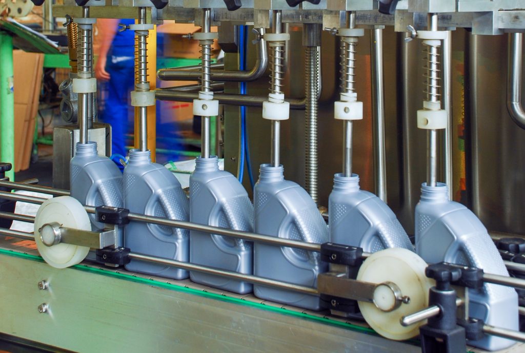 Industrial filling machine with red flexible hoses and blue cables connected to stainless valves and fittings.