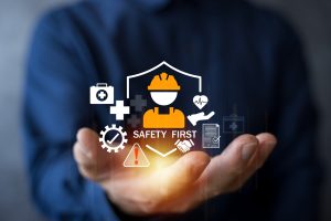 Hands hold a glowing cluster of safety icons (helmet, heart monitor, gears, documents) with the text 'SAFETY FIRST'.